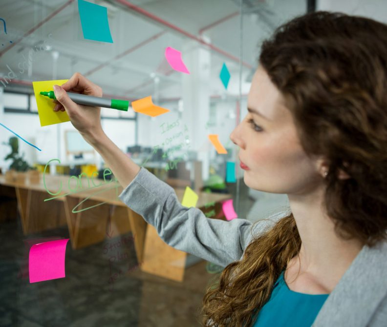 Female executive writing on sticky notes in creative office